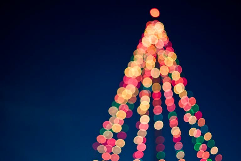 Colorful bokeh lights forming a Christmas tree against a dark blue sky.